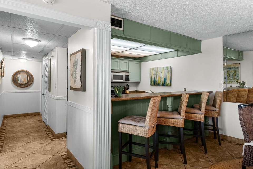 Cozy kitchen bar area with green cabinetry and wicker stools for casual dining.