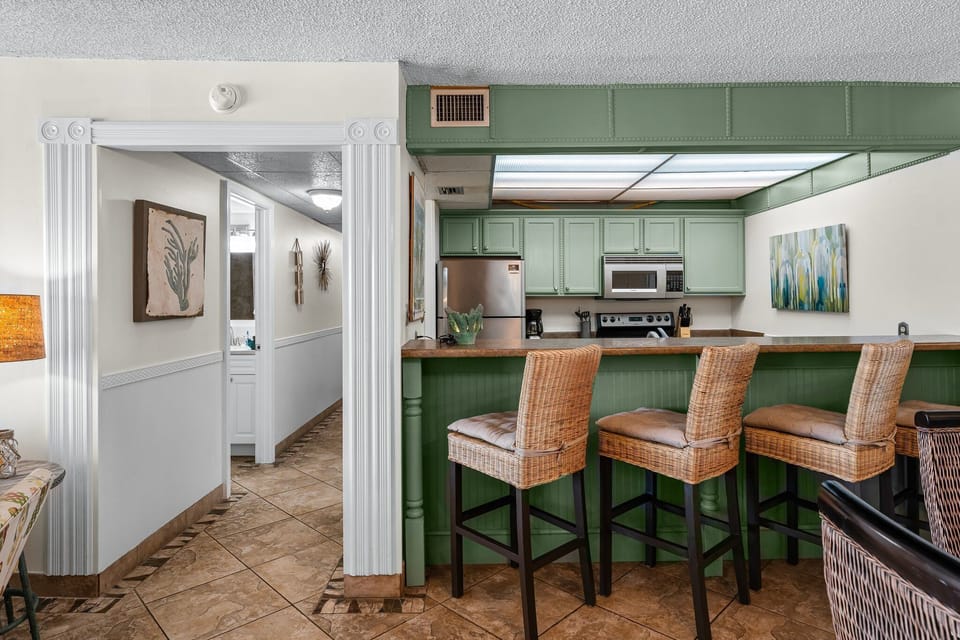 Cozy kitchen with green cabinetry and a breakfast bar with wicker stools