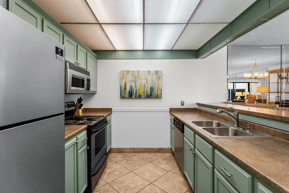 Compact kitchen with green cabinetry and modern appliances.