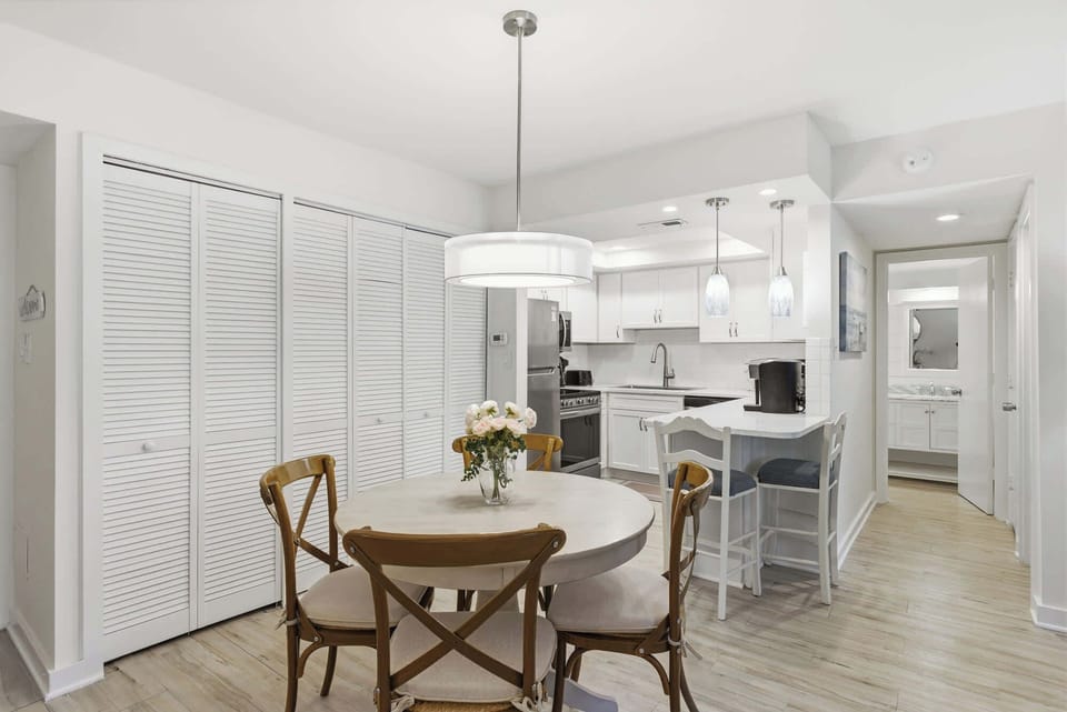 Honey-toned wood chairs surround a circular dining table, creating an intimate nook for morning coffee. Bright white finishes and soft pendant lighting give this open kitchen a clean, airy feel that invites slow breakfasts and easy conversation.