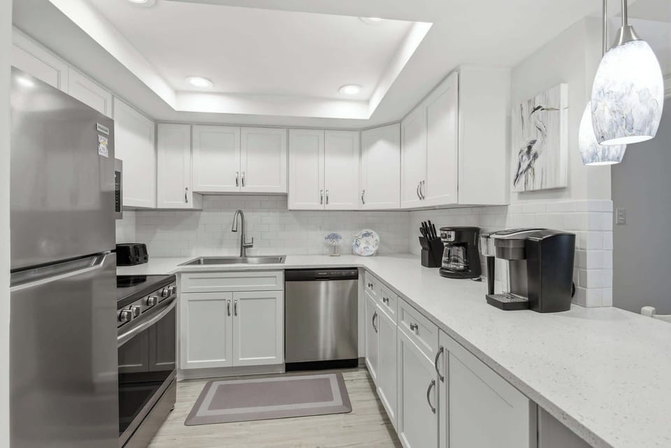 Stone counters and sleek stainless appliances sparkle under soft, recessed lighting in this airy kitchen. Artful pendant lamps and subway tiles create a bright, contemporary space perfectly prepared for your morning coffee and coastal meals.