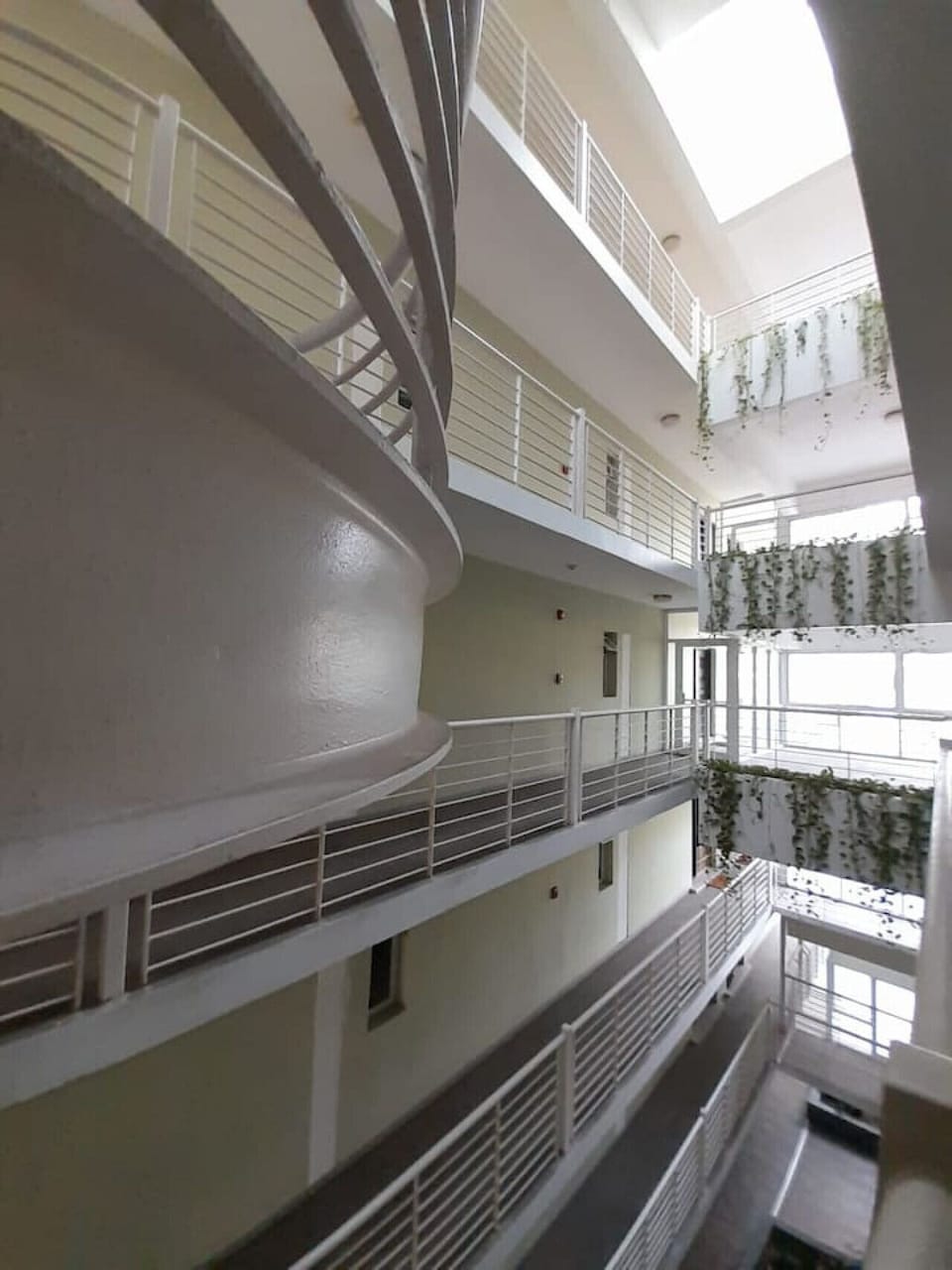 Open-air atrium w/ curved balconies & greenery cascading through the building