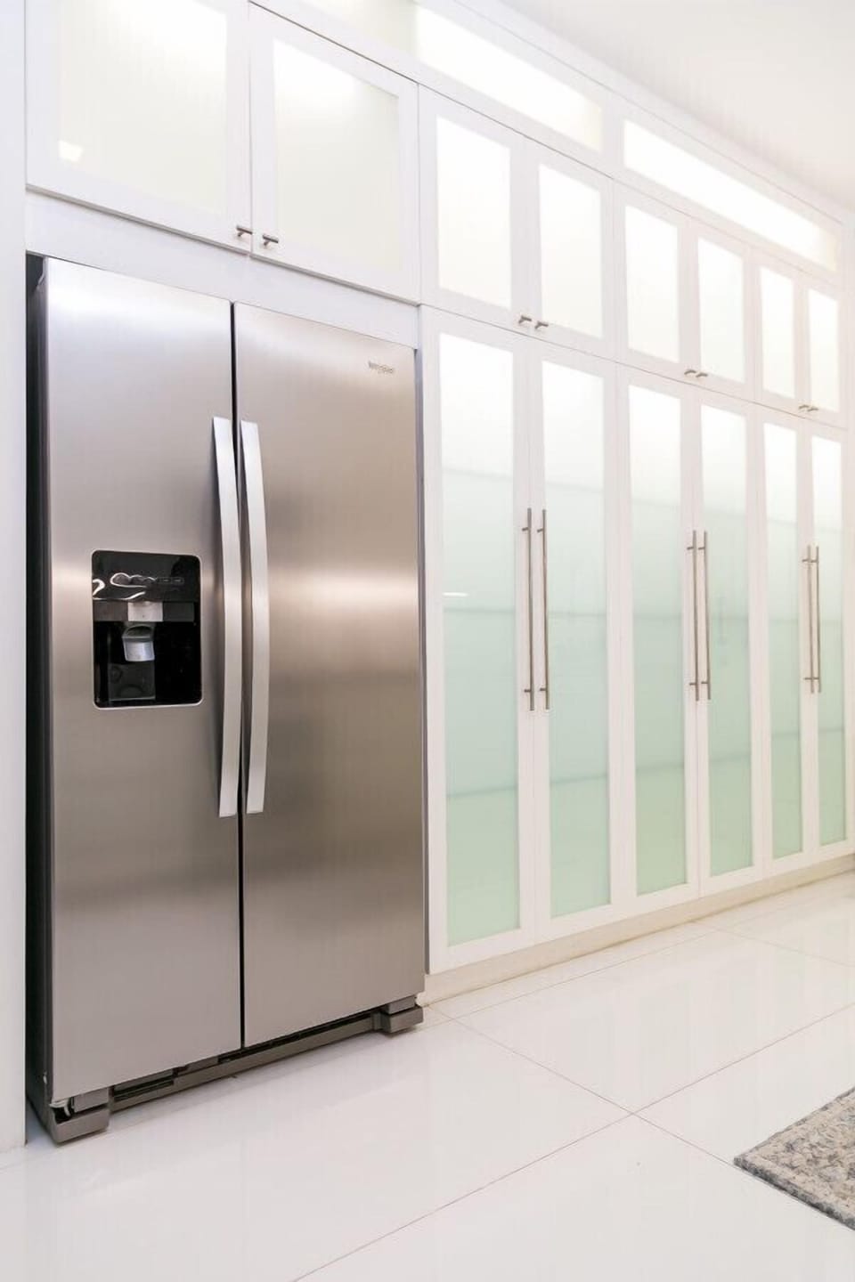 Stainless steel fridge w/ water dispenser beside sleek glass pantry doors
