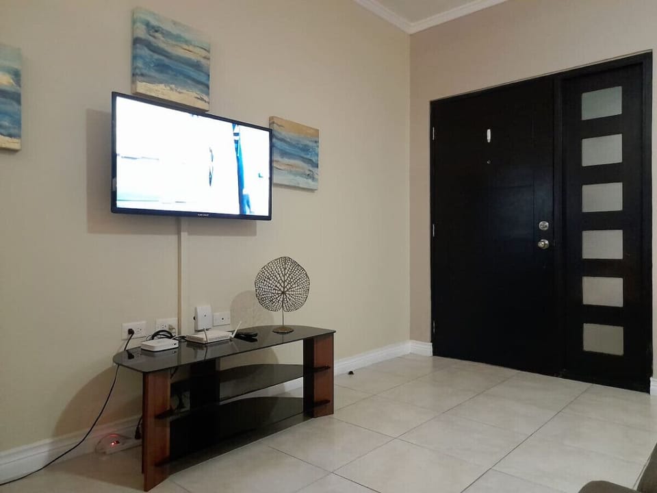 Living area w/ wall-mounted TV, media console & modern entry door nearby