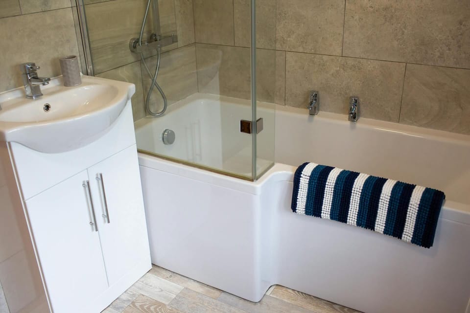 Bath with shower above, hand wash basin with storage under