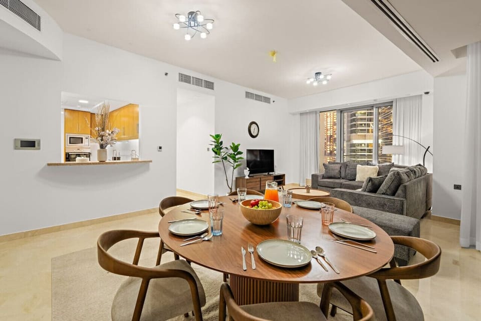 Dining room with an oval wooden table set for six, a fruit bowl, and a view of the living room.