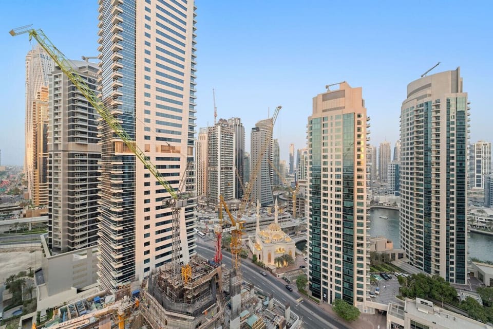 Aerial view of a city with numerous skyscrapers and construction cranes under clear skies.