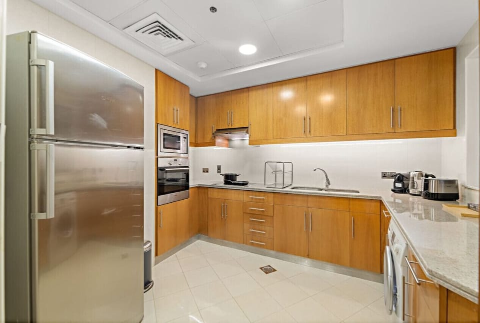 Modern kitchen with light wood cabinets, stainless steel appliances, and tiled floor.