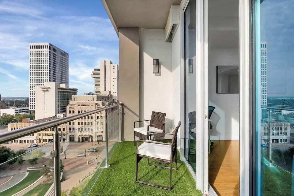 Outdoor balcony with seating, glass railing, and elevated views of the surrounding city.