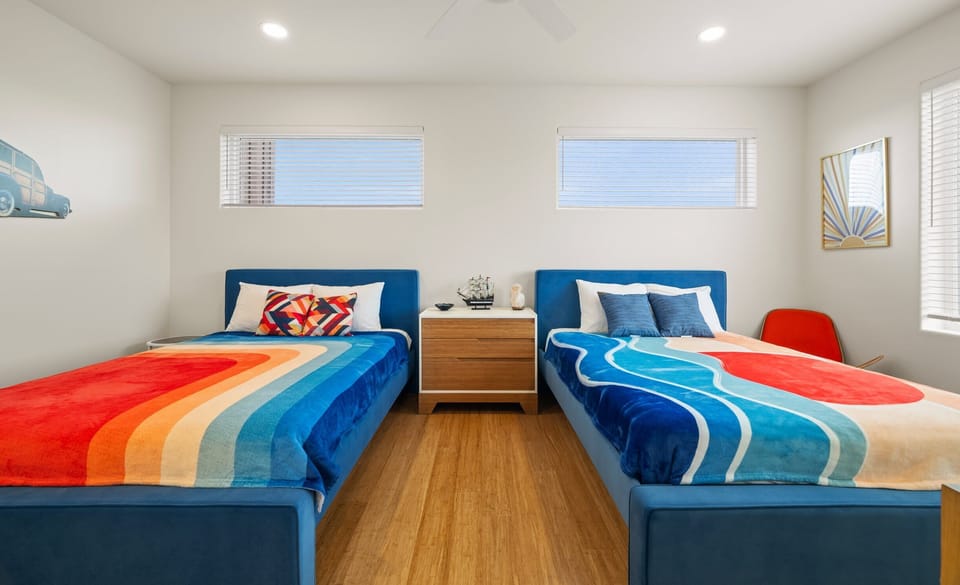 Guest Bedroom — Two Blue Beds with Wave & Sunset Blankets, Ship Model & Sunrise Art