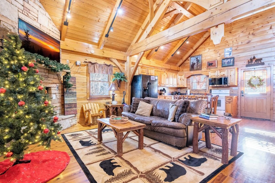 Step into your cozy cabin retreat where rustic wood beams frame comfortable leather seating and a festive tree awaits your holiday memories.