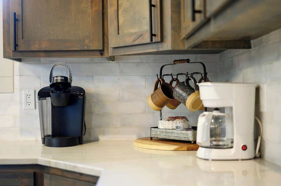 Coffee station with Keurig and drip coffee maker, rustic wood cabinets, and hanging mug rack.