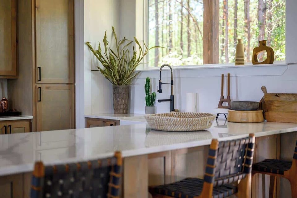 Sleek kitchen corner with large windows, earthy decor, and farmhouse sink—blending modern and rustic design.