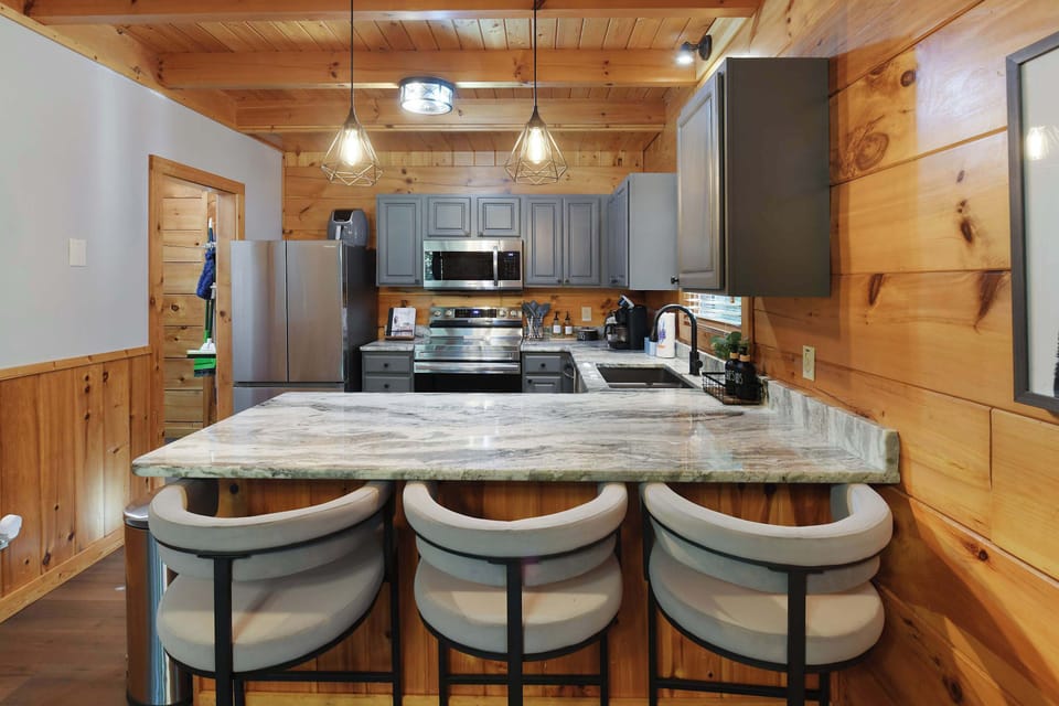 Modern kitchen with marble countertops and gray cabinetry in a rustic wood-paneled setting