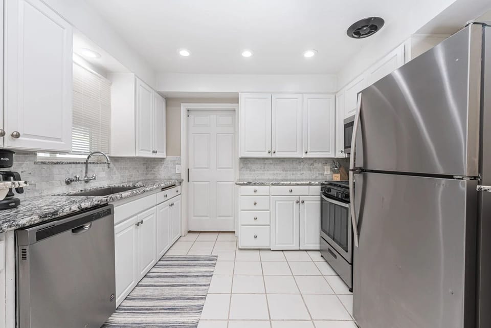 Bright, fully equipped kitchen with white cabinetry, granite counters, and stainless steel appliances for easy vacation meal prep
                