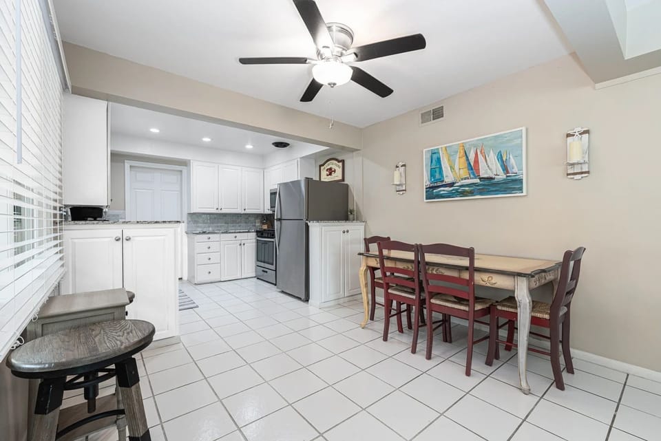 Open dining and kitchen layout with tile flooring, ceiling fan, and convenient access to full kitchen amenities
                