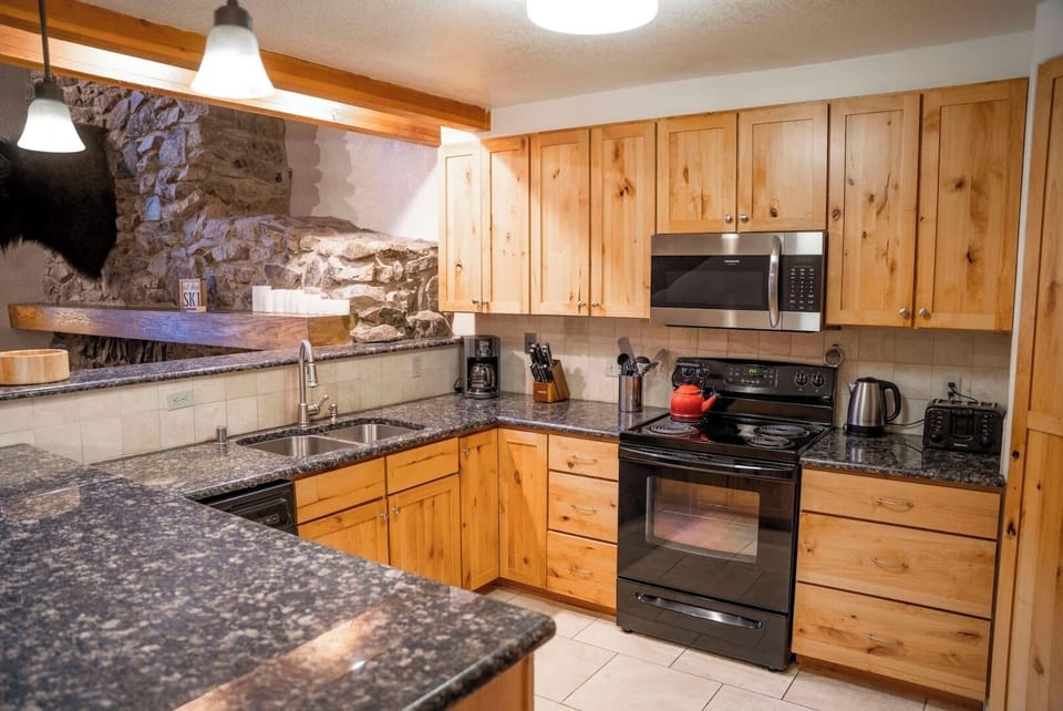 Prepare your favorite meals in this fully equipped kitchen with granite countertops, stainless appliances, and rustic stone accent wall adding mountain charm to your culinary experience.