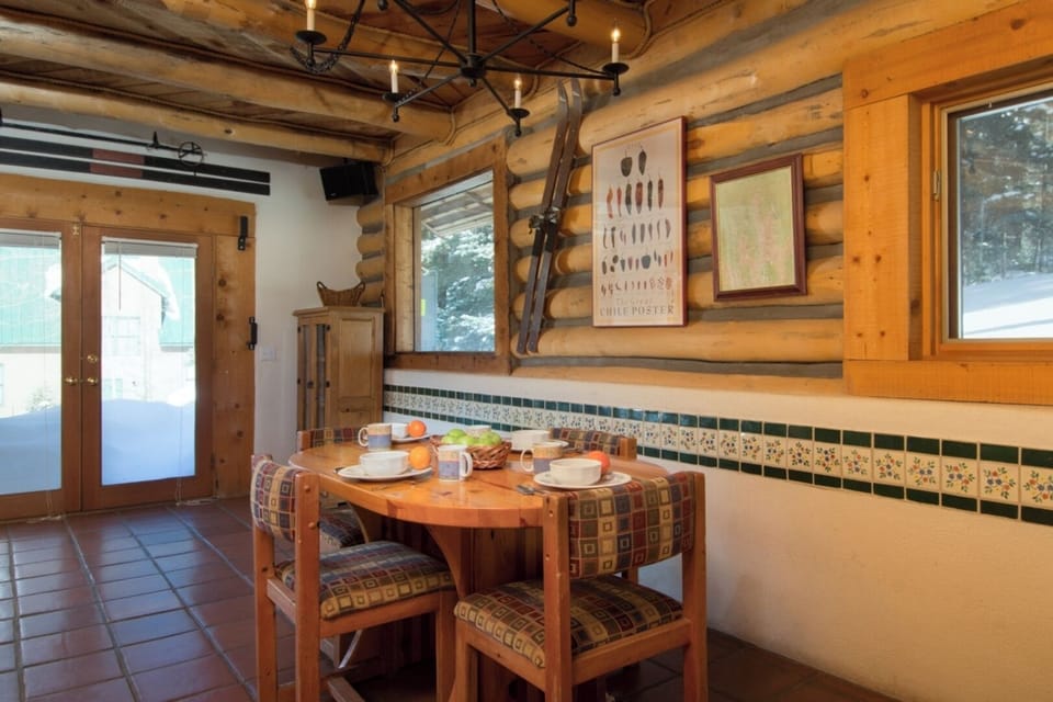 Gather around this inviting dining table where warm wood tones and rustic charm set the stage for memorable meals. Sunlight streams through windows framing snowy views beyond.