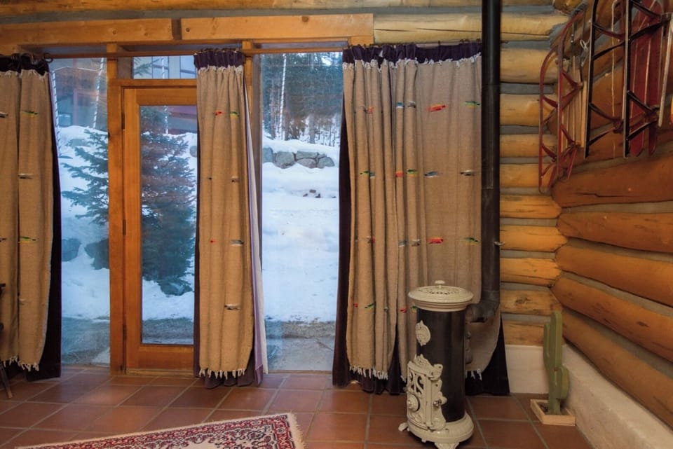 Step inside your cozy log cabin retreat and glimpse a serene winter wonderland through the large windows—snow-covered trees and peaceful nature await just beyond your rustic threshold.
