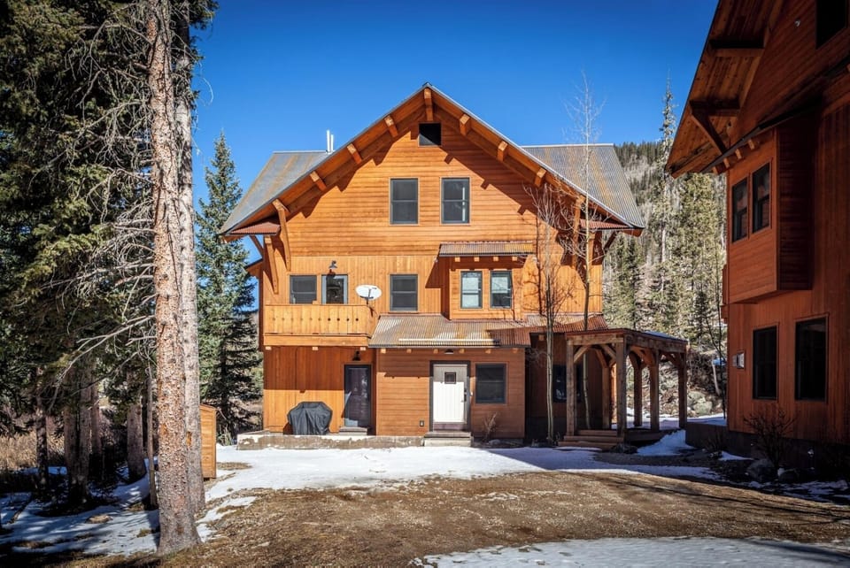 Rustic mountain lodge featuring warm wood construction, nestled among towering pines with scenic mountain backdrop. Private outdoor space with covered porch and yard area.