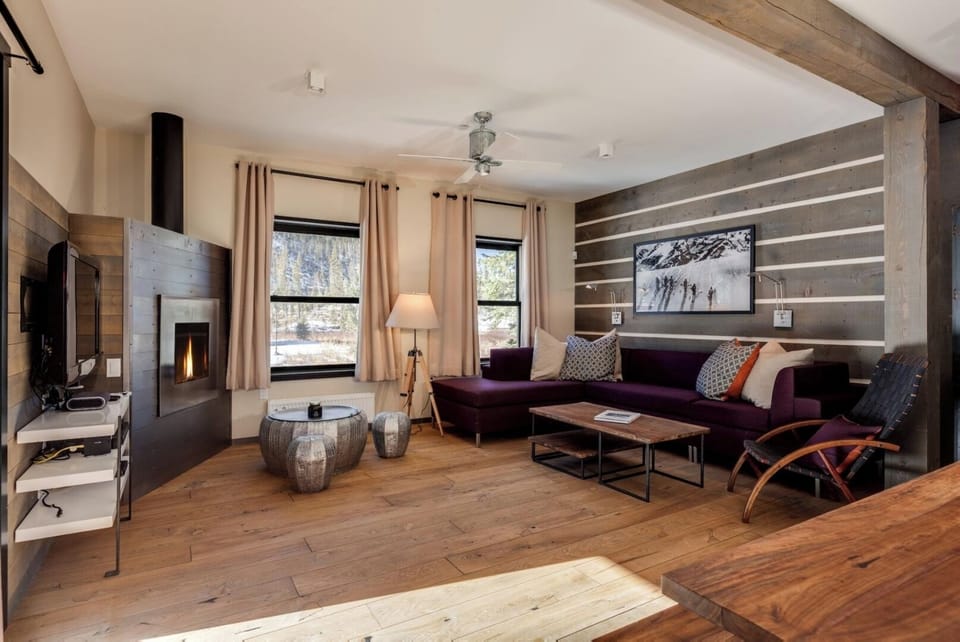 Sink into the rich plum sofa by your own gas fireplace, savoring wood beam charm, open shelving for your books, and soft natural light from oversize windows.