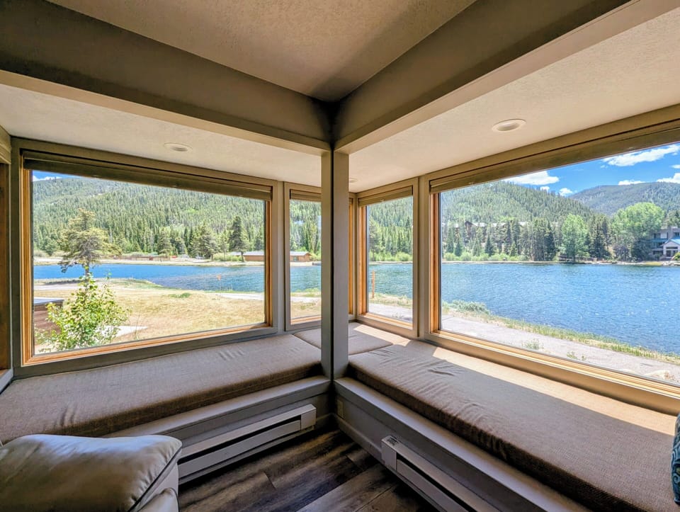 Picture yourself curled up in this cozy window nook, where cushioned bench seating frames breathtaking views of the lake and forested mountains beyond—your perfect spot for morning coffee or quiet reflection.