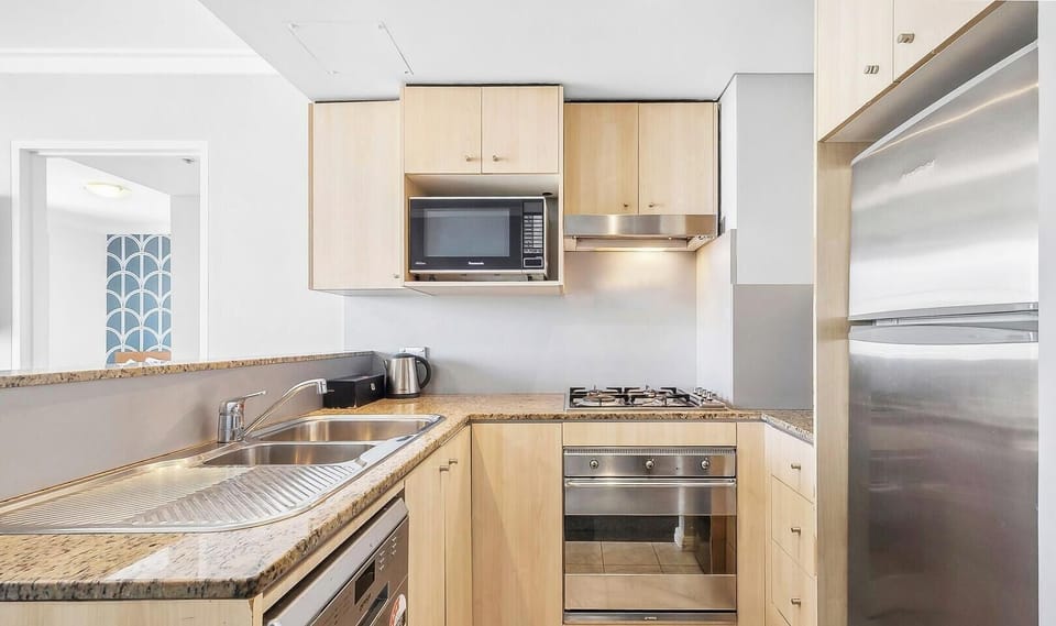 A clean, U-shaped kitchen layout with light wood cabinetry, granite-style countertops