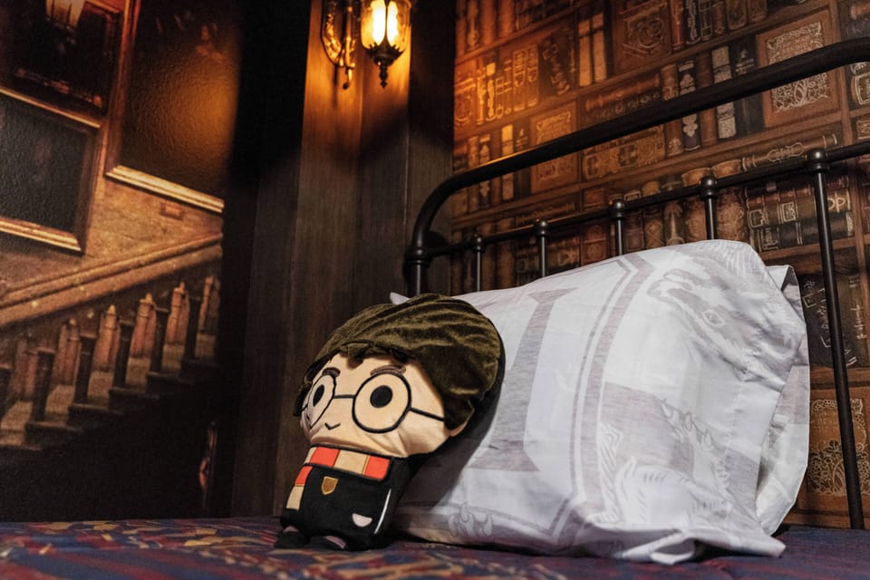 Enjoy a whimsical bedroom featuring rich library-like wallpaper that creates a cozy atmosphere. A charming plush character by a crisp white pillow adds a playful touch to the inviting bedspread and warm lighting for your stay.
