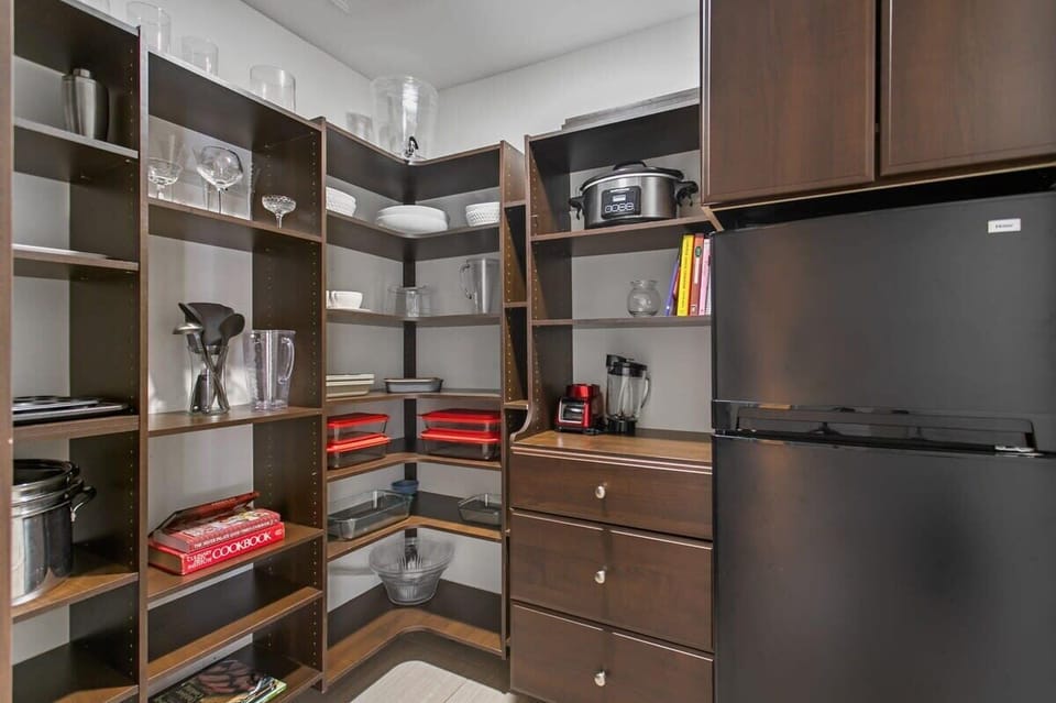Large butlers pantry with serving platters, kitchen appliances, food storage containers, cookbooks, and an  additional fridge/freezer