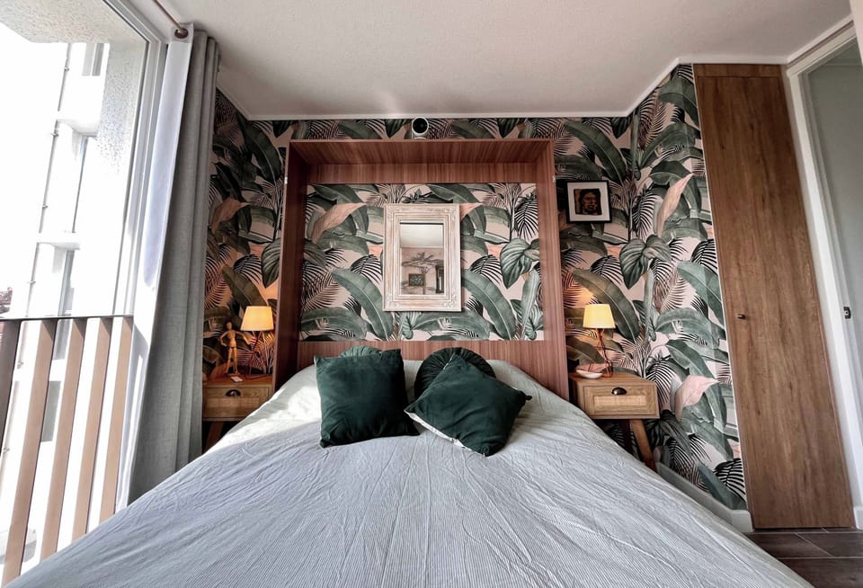 Bedroom with double bed, leaf-print accent wall and bedside lamps