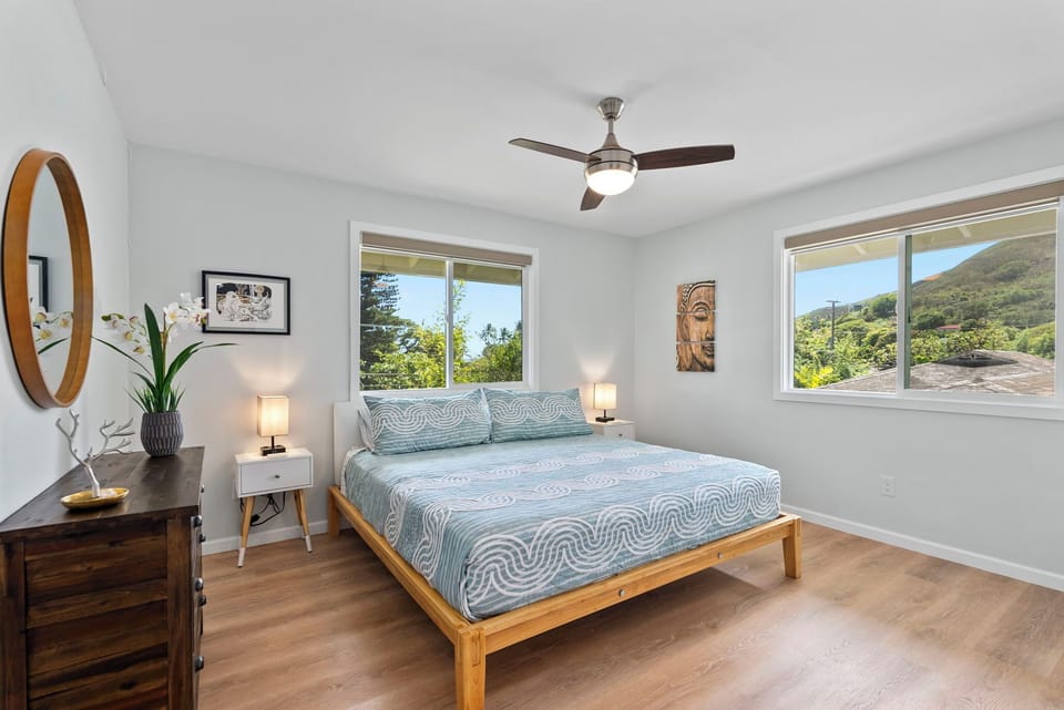 Relax in this serene guest bedroom featuring a light and airy decor, framed by nature views from the surrounding windows.