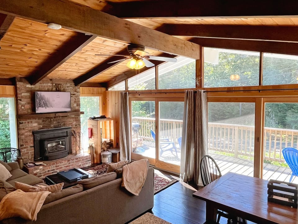 Bright and cozy living room with vaulted ceilings, wood-burning fireplace, Roku TV, and access to the large deck—perfect après-ski gathering space just minutes from Mount Snow.