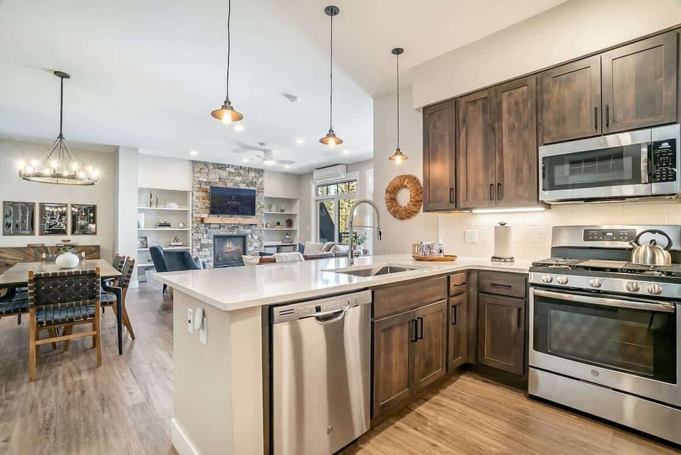 Bright open-concept kitchen with stainless steel appliances, island seating, and dining for 6—flowing seamlessly into the cozy living room.