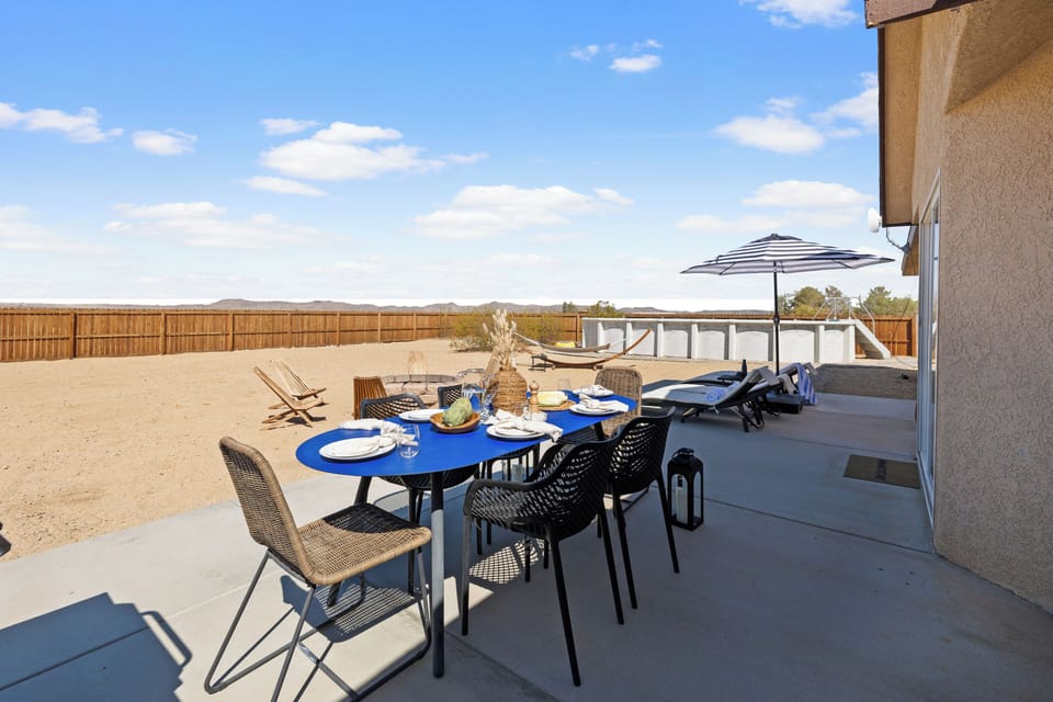Outdoor dining area set for a sunny meal beside loungers, hammock, and pool.