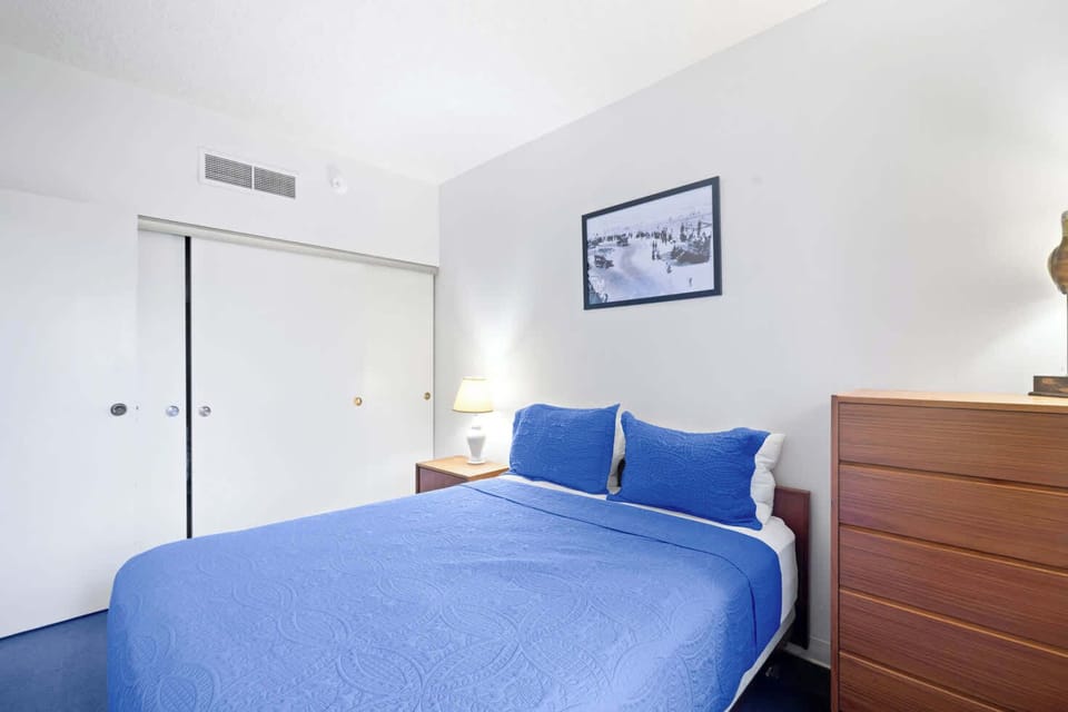 Cozy bed, ample storage with a sleek wooden dresser and built-in closet, warm lighting, and a minimalist design perfect for relaxation.