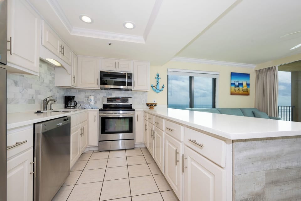 This modern kitchen features stainless appliances, a coffee maker, and a beautiful view of the beach through large windows