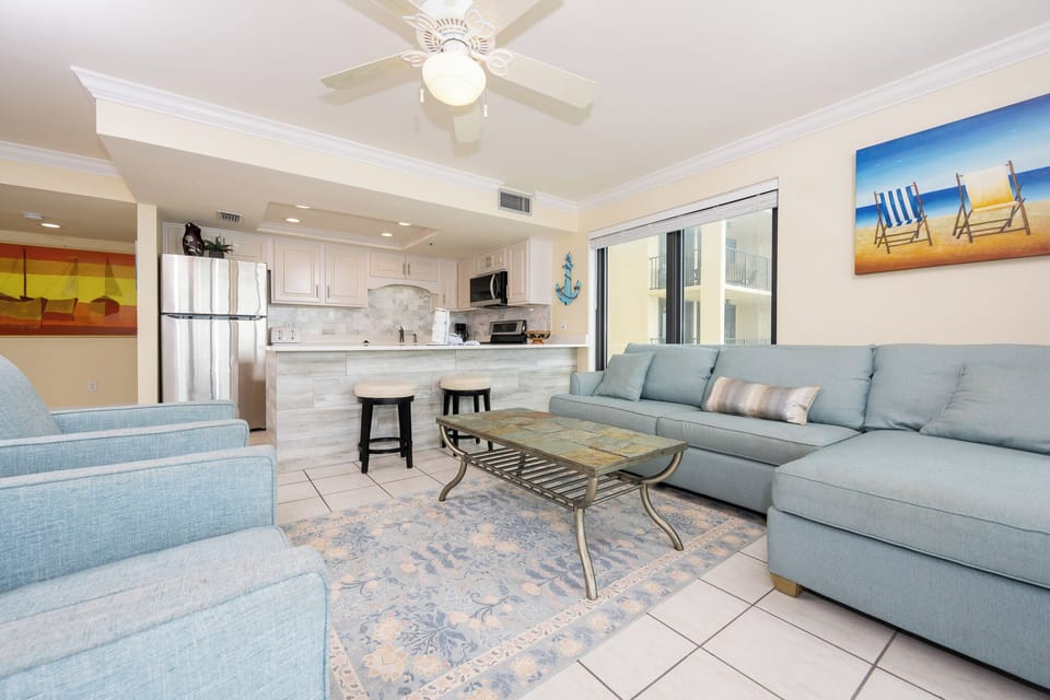 This inviting living area features a cozy blue sectional, a stylish coffee table, and a view of beach chairs on the wall art