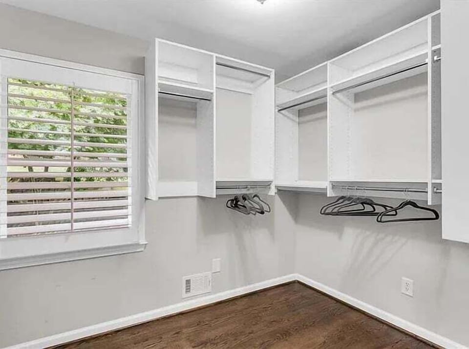Walk-in closet with built-in white shelving, hanging rods, hardwood floor, and a window.