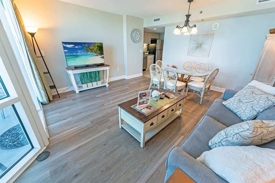 - Open concept living space with a cozy sofa and a smart TV for entertainment - Enjoy meals at the dining table or unwind with a movie after a day at the beach - Thoughtfully decorated with warm tones, wood flooring, and plenty of natural light