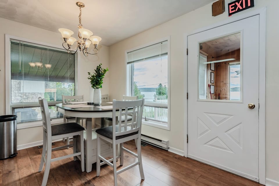 This charming dining space, situated right by the window, offers stunning panoramic views of the lake. Whether you're enjoying a meal or sipping your morning coffee, the natural beauty outside provides the perfect backdrop. The simple yet elegant table setup makes it a delightful spot for any occasion.