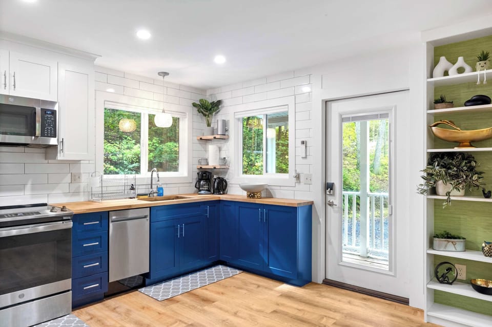 Modern kitchen with blue cabinetry, stainless steel appliances, and natural light from large windows.