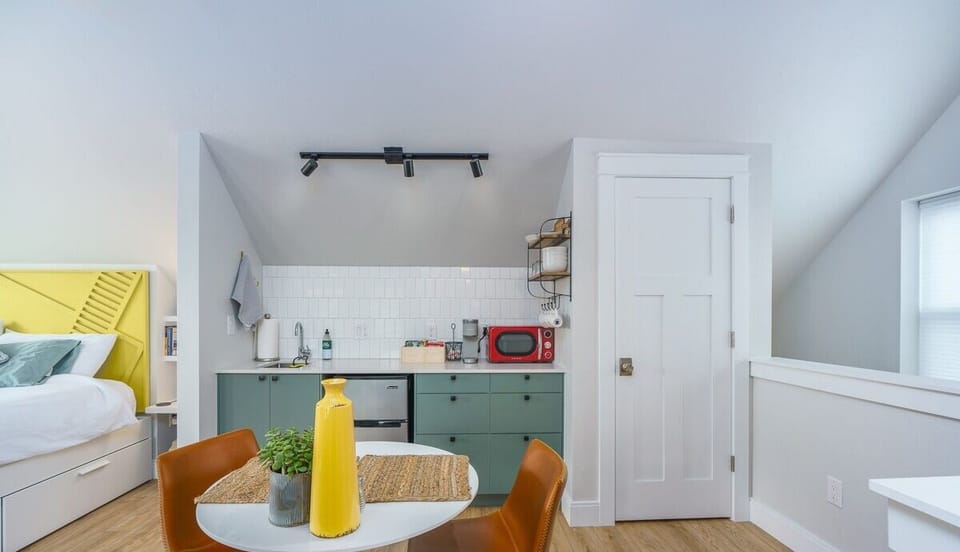 - Cozy eat in space with two leather chairs, a round table, and a cheerful yellow vase centerpiece
- Compact kitchenette offers a microwave, sink, mini fridge, and coffee station
- Stylish modern layout with soft lighting and light wood floors