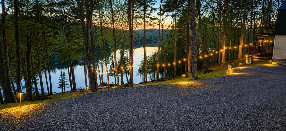Lakefront cabin setting with string lights, wooded surroundings, and stunning sunset views over the water.