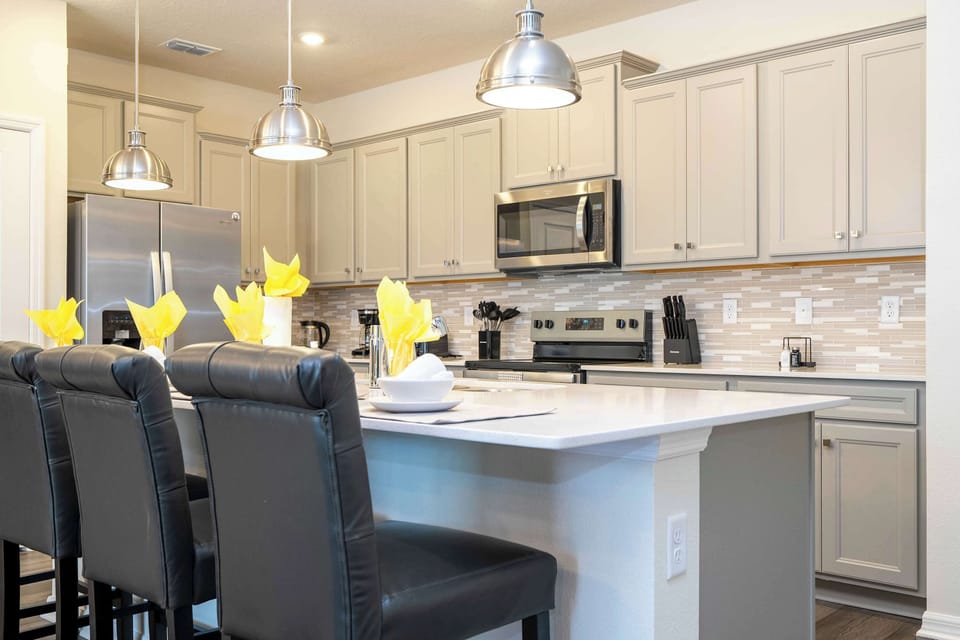 Sip your morning coffee at the cozy island bar with three plush leather stools under industrial-chic pendant lights! This modern kitchen shines with quartz counters, stainless steel appliances and a stylish mosaic tile backsplash.