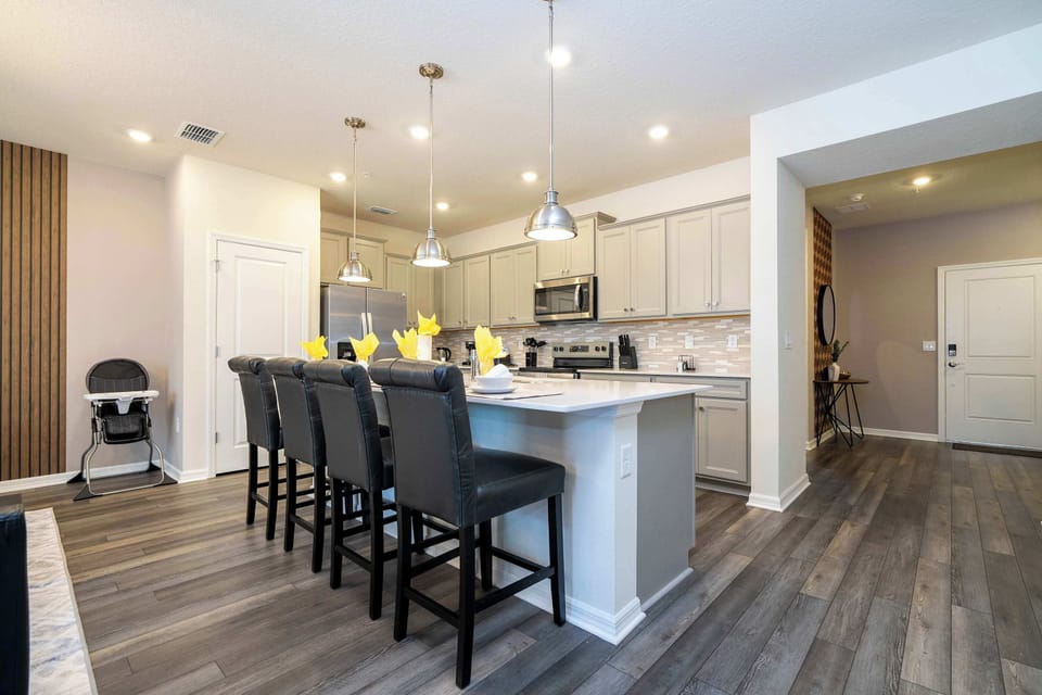 Gather around the quartz-topped island with four comfy bar stools under sleek pendant lights! This open-concept modern kitchen features stainless appliances, gray cabinetry and wood accent details-perfect for cooking & conversation.