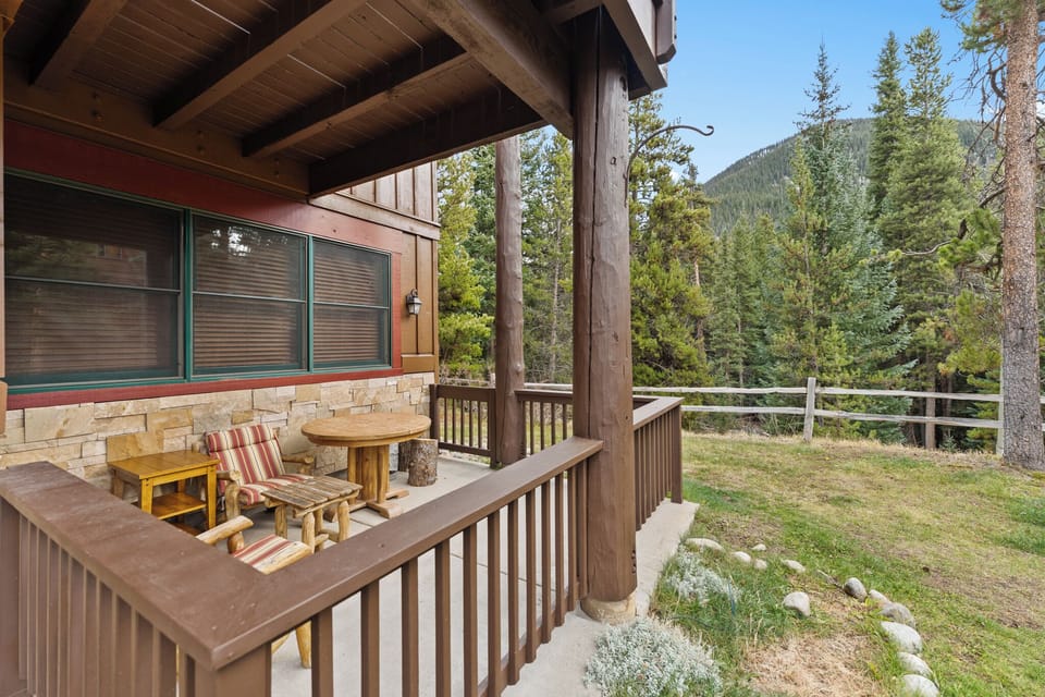 A covered deck with rustic charm features wooden seating perfect for morning coffee while taking in the forested mountain backdrop.