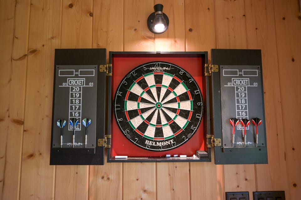 A spacious game room featuring a large TV, darts, a pool table with ping pong conversion, and a stunning custom bar.
