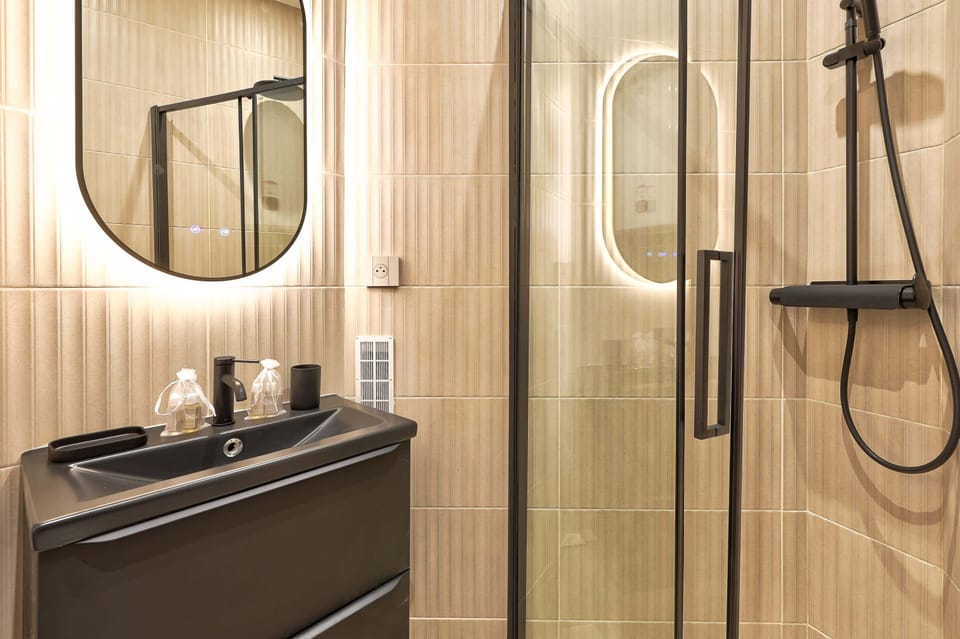 La salle de bain du studio allie modernité et sobriété, avec des finitions en céramique blanche et des touches métalliques élégantes. Une douche à l'italienne, un lavabo minimaliste et des rangements astucieux