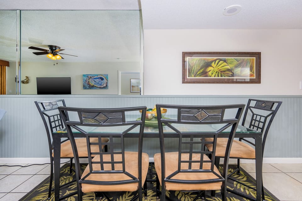 Bright dining area with a glass table, stylish chairs, and tropical artwork, perfect for enjoying meals together