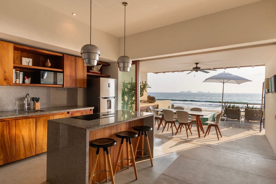 A fully equipped, open-air kitchen with stylish bar seating, elegant wooden finishes, and panoramic ocean views.